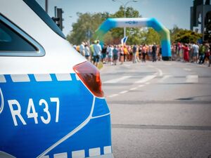 Radiowóz policyjny podczas zabezpieczenia biegu oraz uczestnicy.