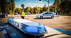 Policjant oraz dwa radiowozy w trakcie zabezpieczenia przejazdu.